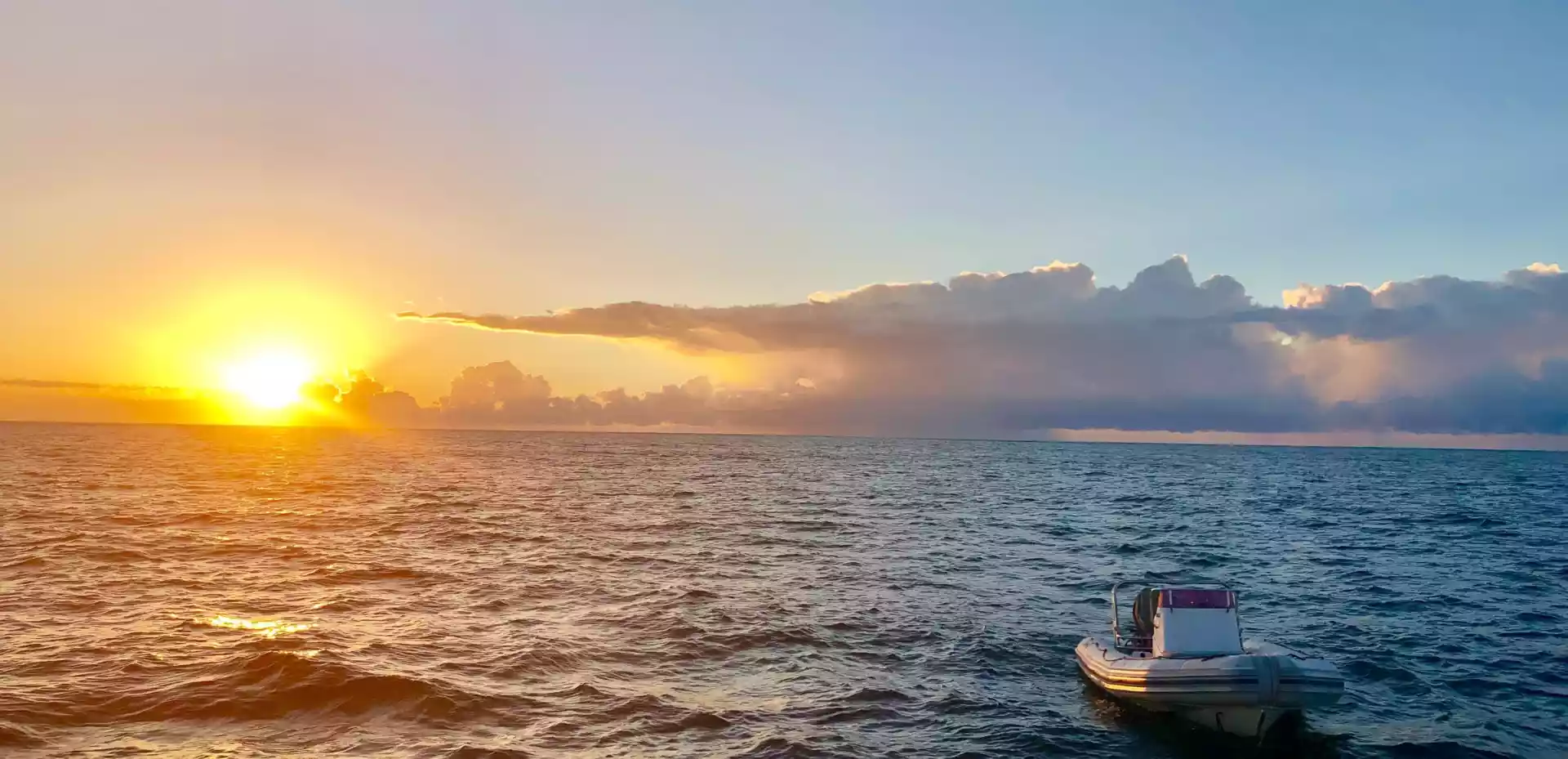 Liten hvit båt flyter på det rolige havet i Mosambik under en vakker solnedgang med oransje og rosa nyanser i himmelen.