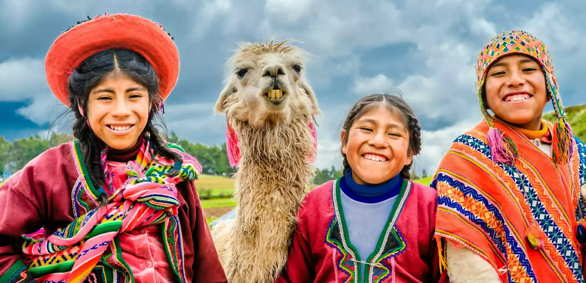 Tre medlemmer av urbefolkningen i Ecuador smiler mot kameraet vedsiden av en med lama.