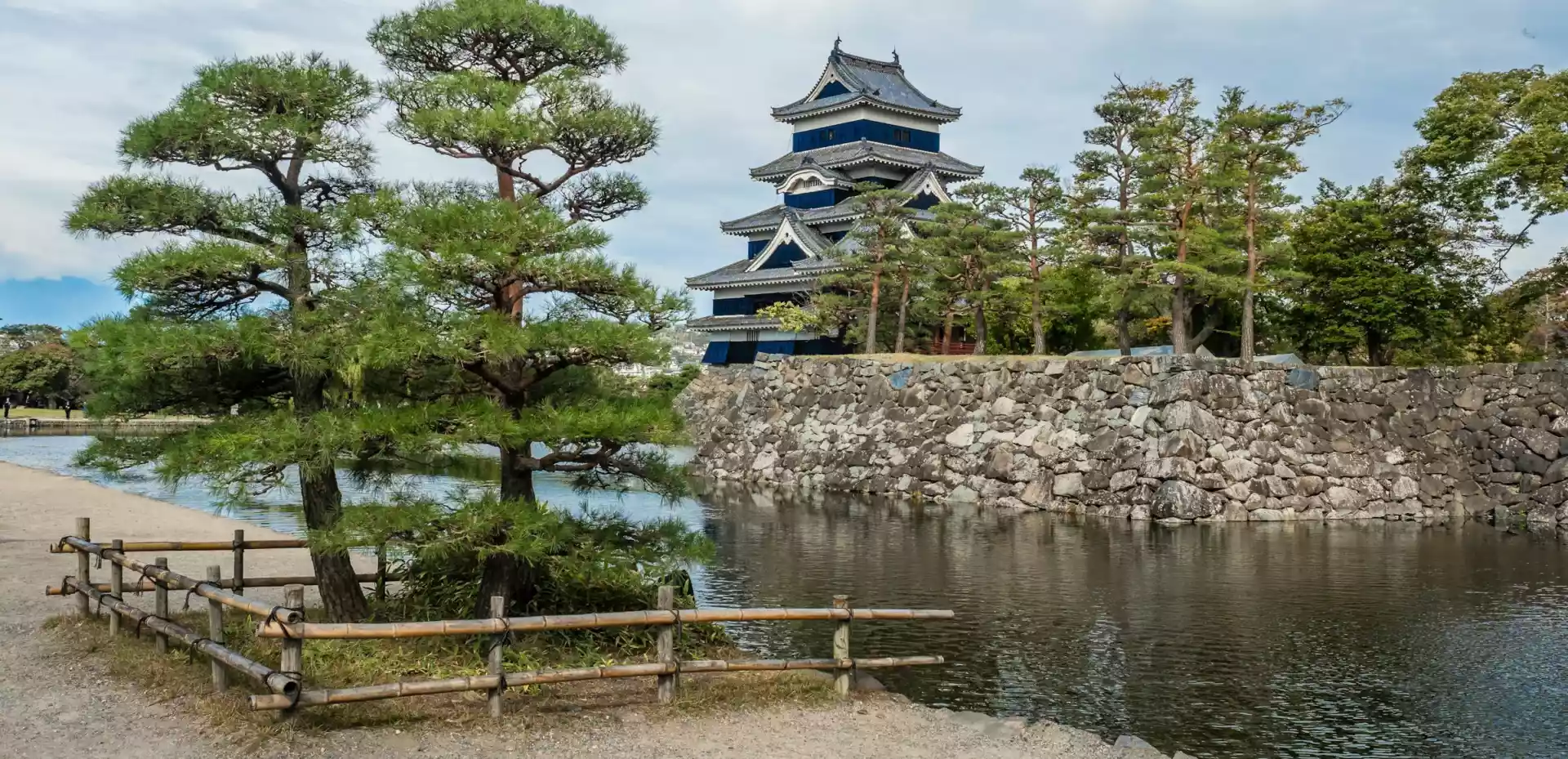 Slott i Matsumoto i tradisjonell japansk stil ved en innsjø omgitt av trær.