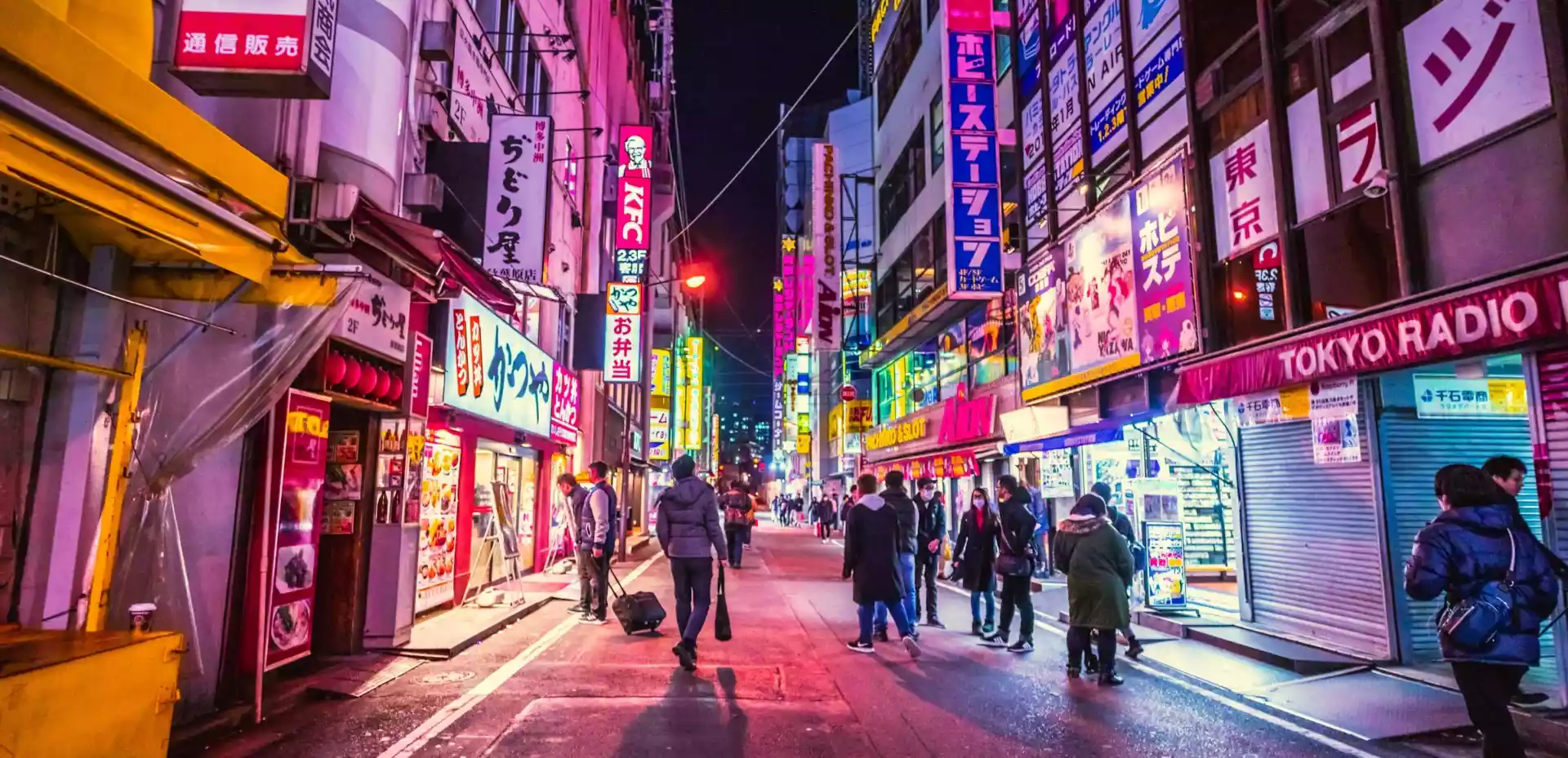 En travel gågate i Tokyo, fylt med mennesker som går forbi under det blendende skjæret av neonlysene som lyser opp den moderne arkitekturen rundt dem.