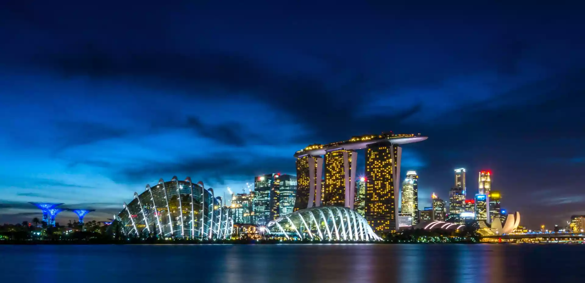 Skyline av Singapore, med mørkt hav og mørk himmel i bakgrunnen.