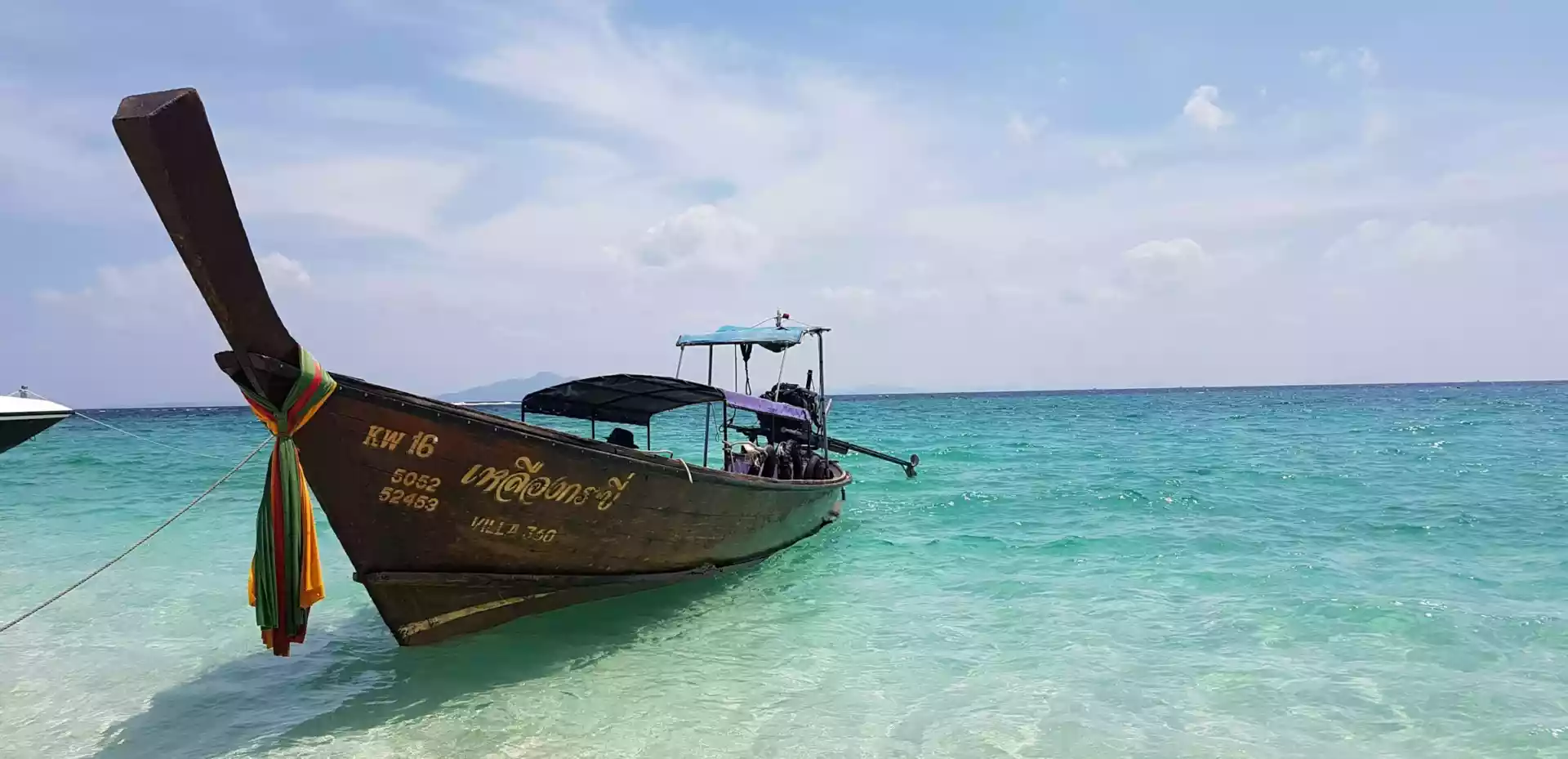 En båt på en strand i Thailand med hvit sand og asurblått, klart hav.