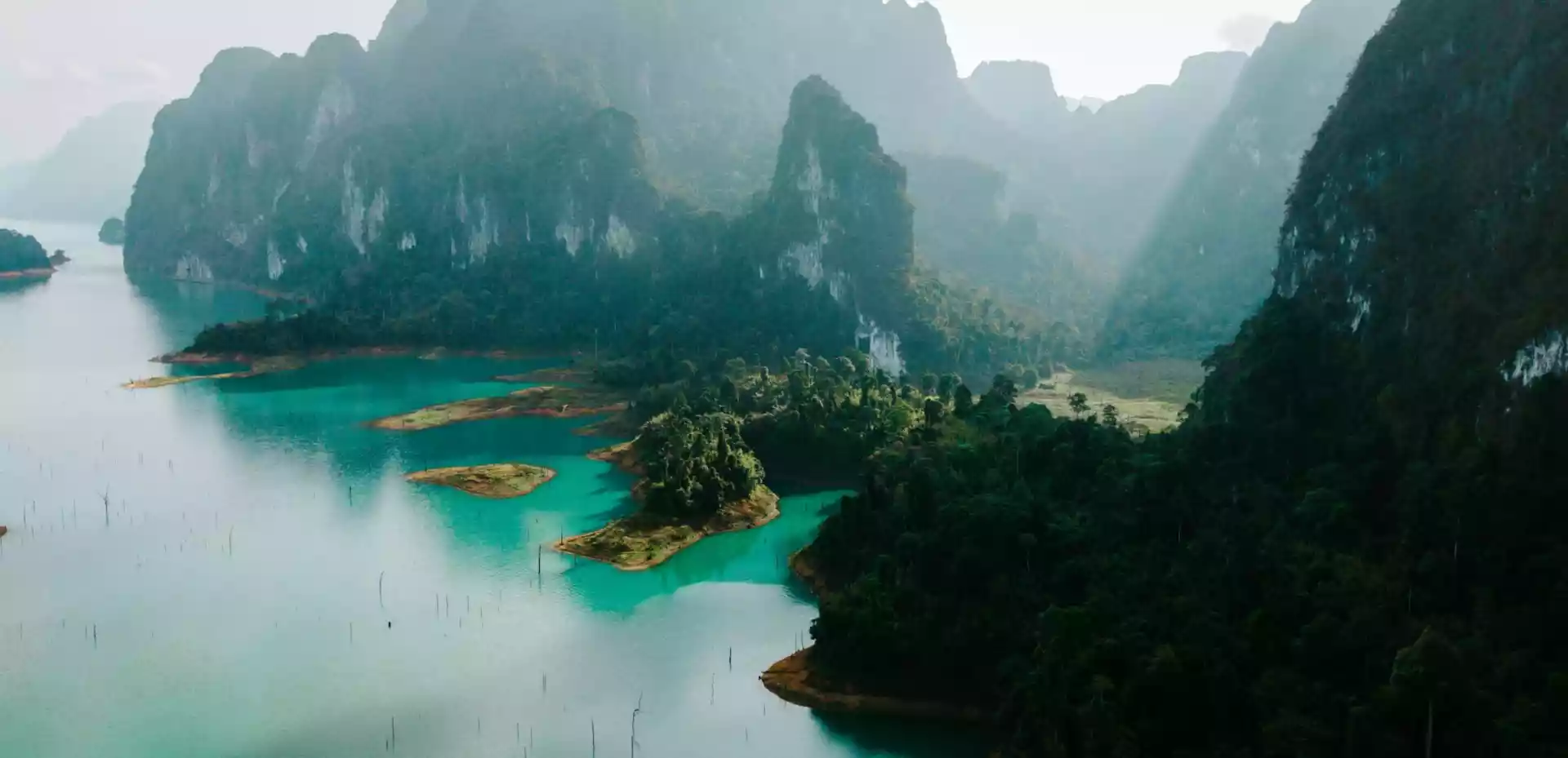 Vakker kystlandskap i Thailand med høye, frodige fjell og klart, grønnblått hav.