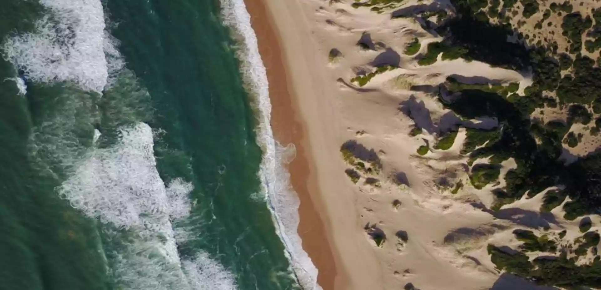 Et overblikk over den fortryllende stranden ved Dunes de Dovela. Med hvite bølger som kruser seg langs kysten og det endeløse blå havet i horisonten, er dette et paradis for avslapning og eventyr.