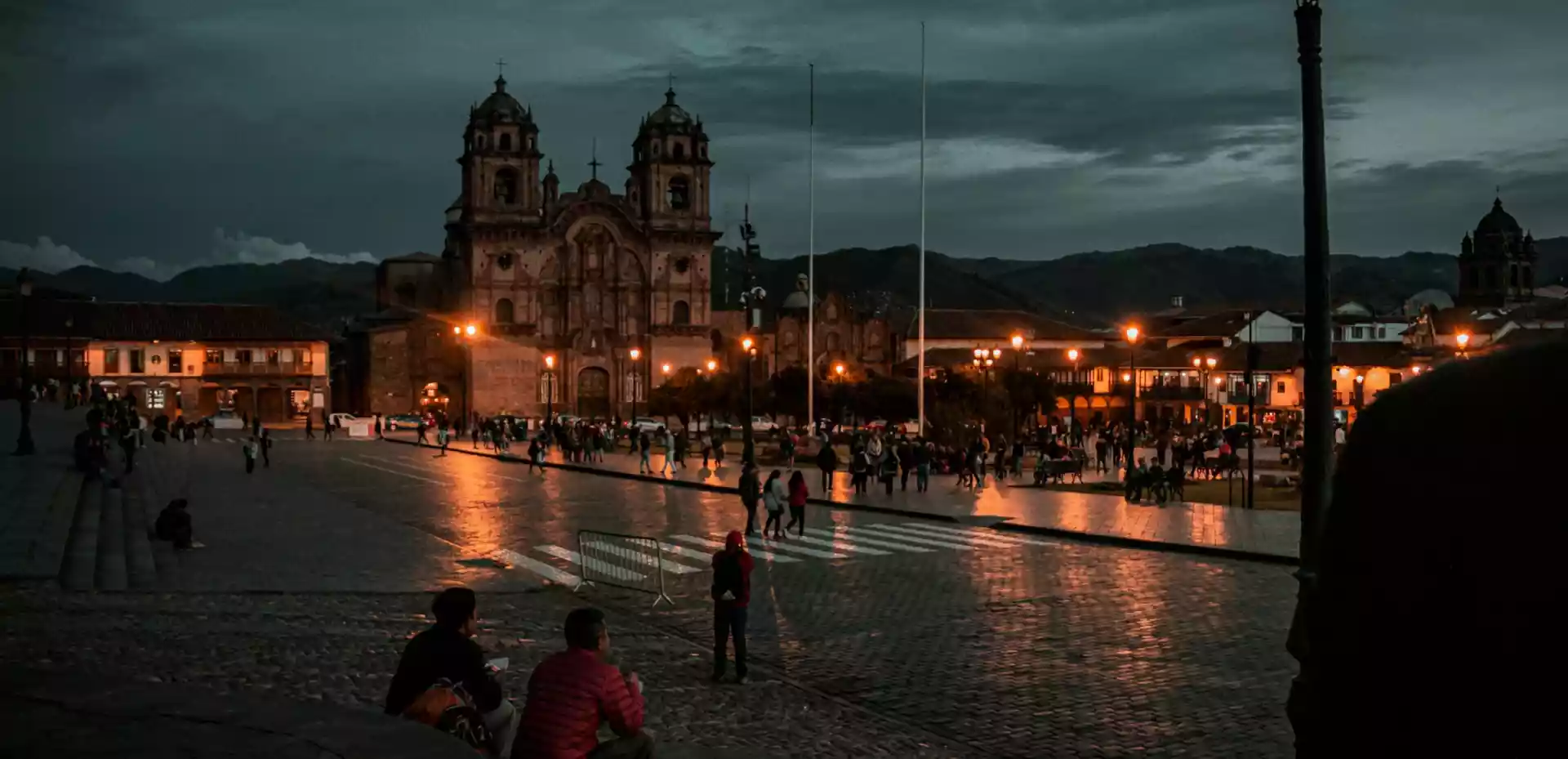 En bygning i barokkstil i Cusco om natten, opplyst av oransje lys fra gatelys. De varme lysene fremhever de intrikate detaljene og den elegante arkitekturen til bygningen, og skaper en atmosfærisk og stemningsfull scene.