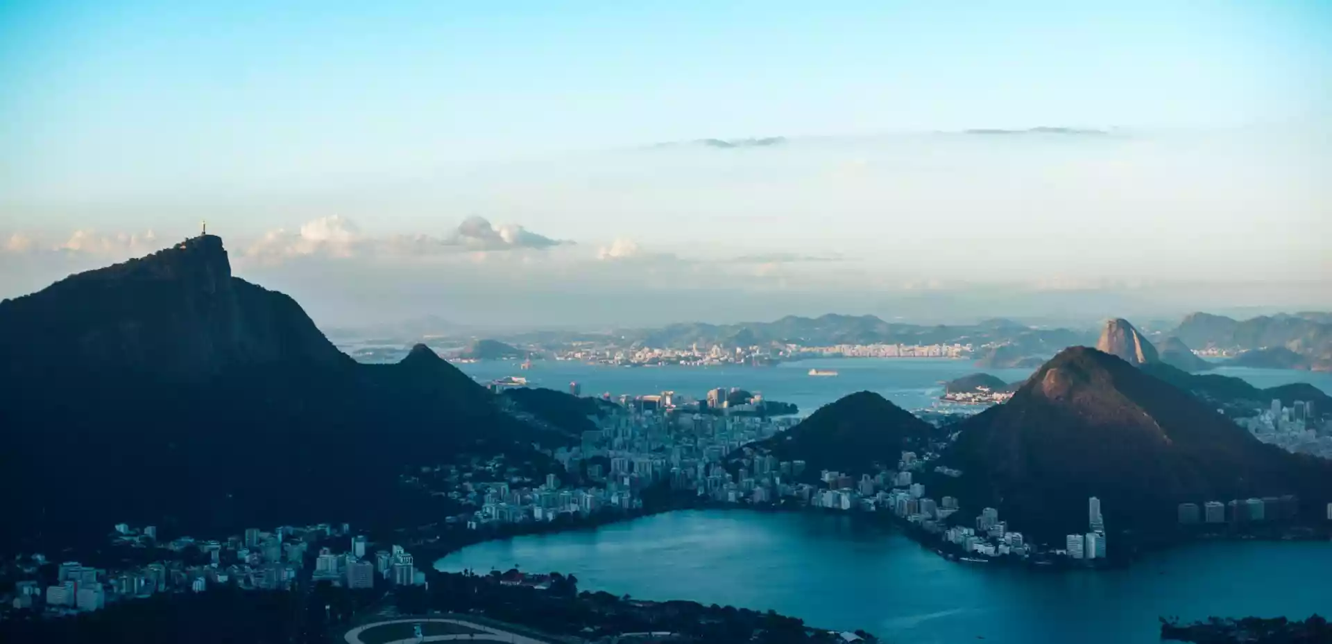 Et overblikk over Rio de Janeiro. Mørke fjell stenger for kveldslys og kaster en skygge over de bygningene og havnen.