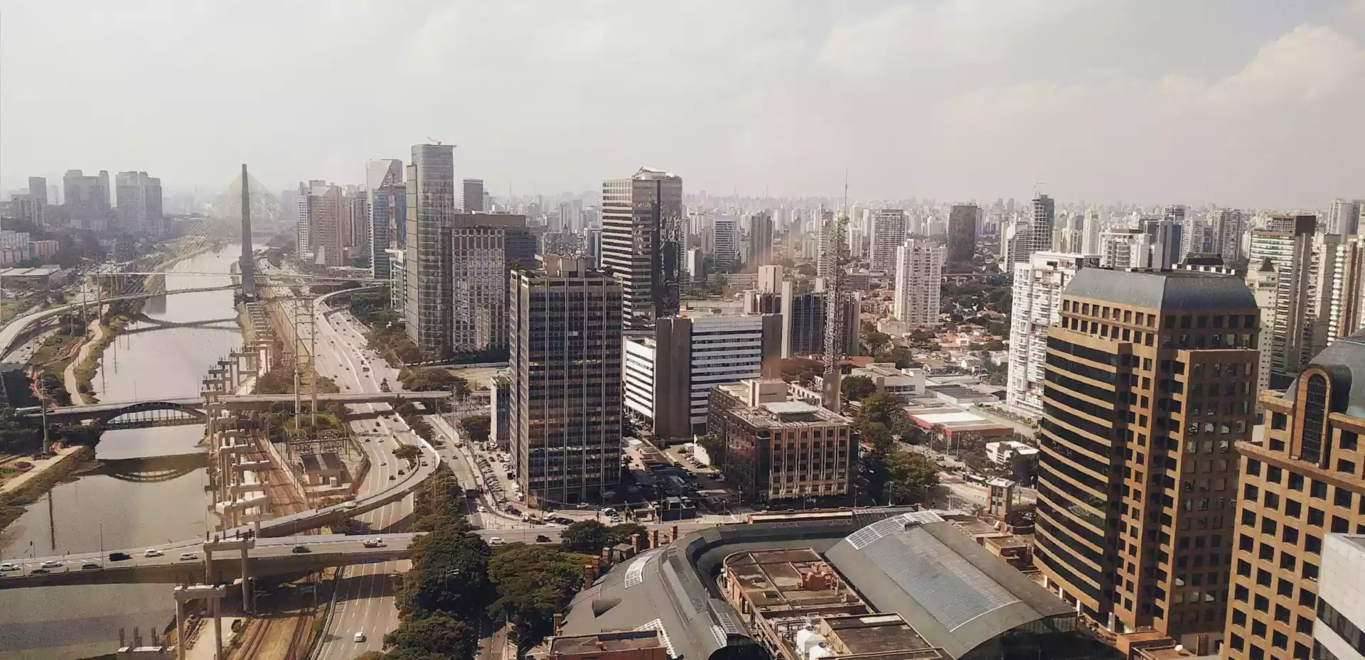 Overblikk over São Paulo. Byen er dekket av høye sementblokker, en elv går igjennom byen, med broer som krysser elven. Himmel er grå.