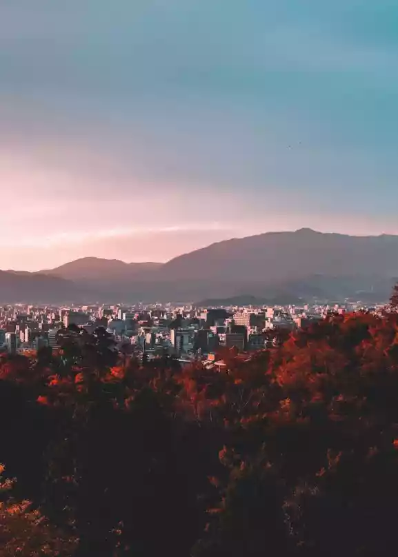 Utsikt over fjell, med en oransje solnedgang, med japansk natur og arkitektur i forgrunnen.