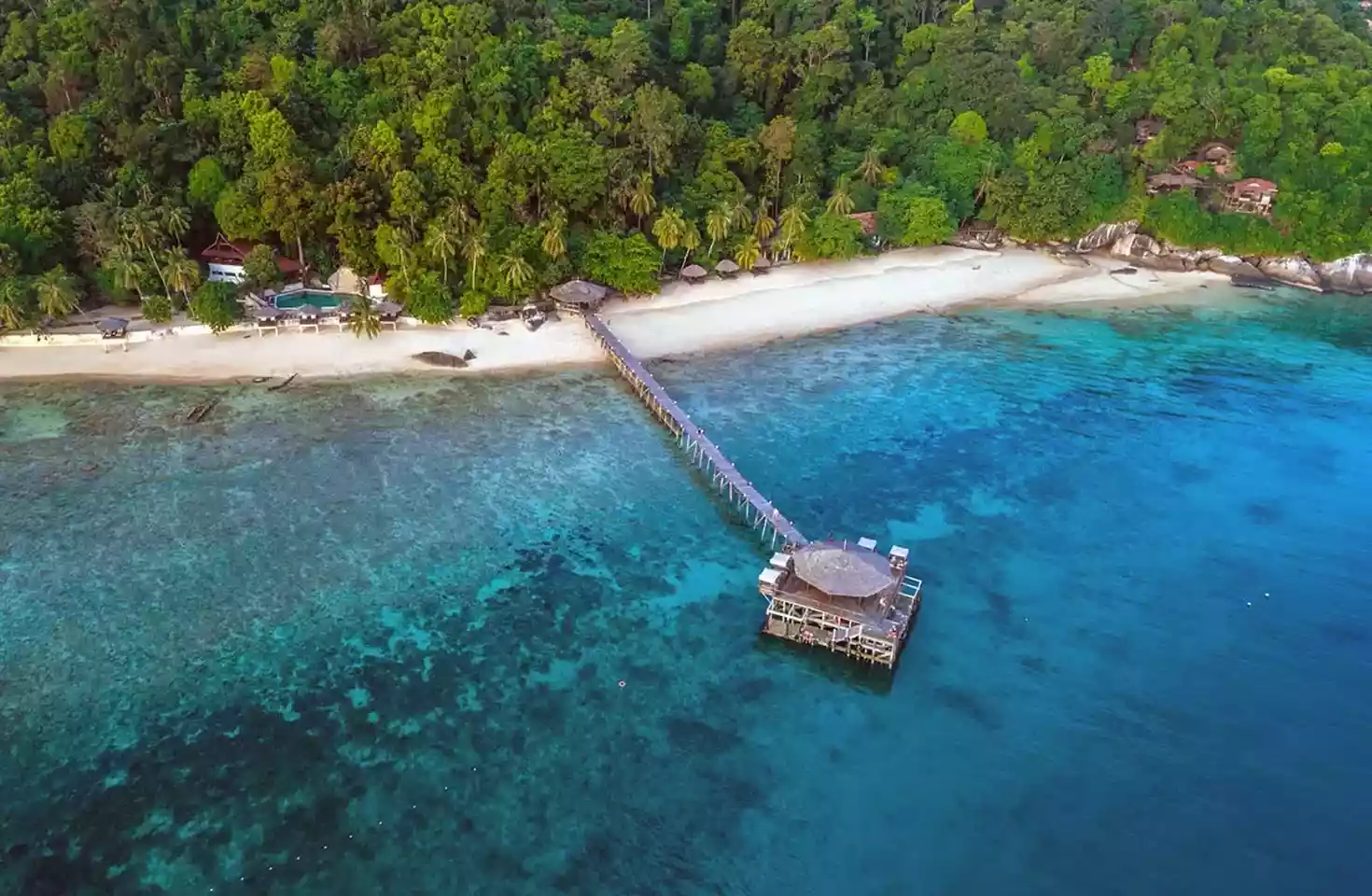 Overblikk over Japamala Resort. En bygning på et blått hav med en gangbru til en strandlinje og frodig skog, med tre bygninger i skogen.