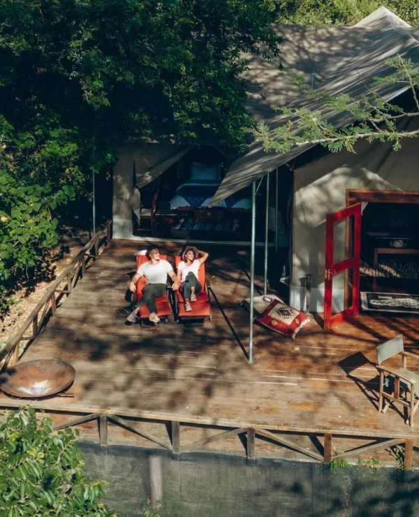 Instinct of Mara sin bungalow omgitt av frodig natur, med to mennesker som slapper av i solstoler ute på altanen.