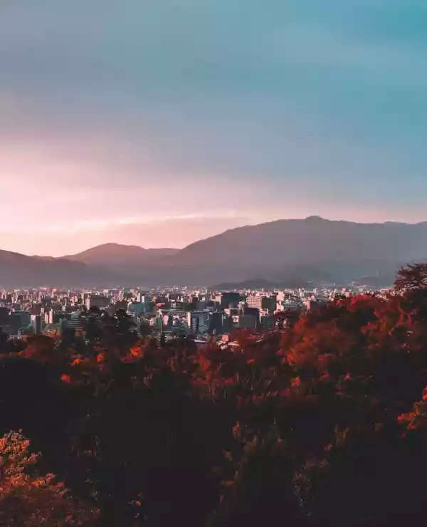 Utsikt over fjell, med en oransje solnedgang, med japansk natur og arkitektur i forgrunnen.
