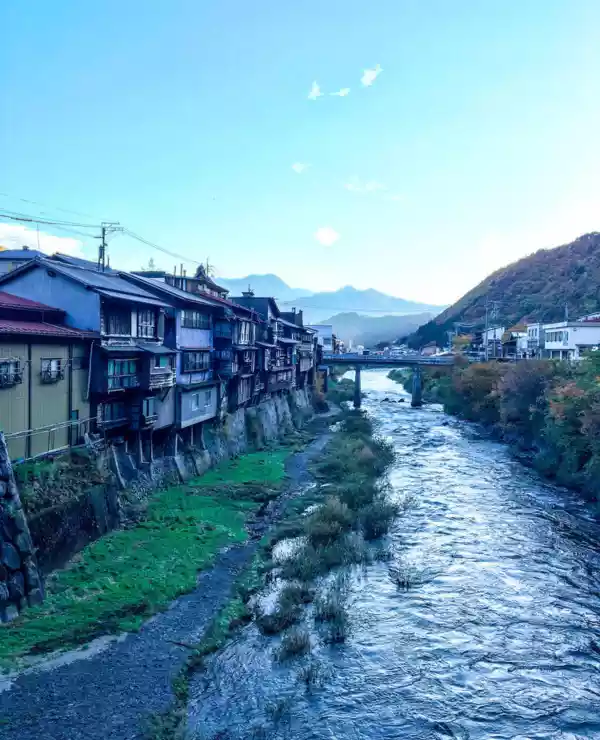 En elv som renner gjennom en liten landsby i Japan. Blå himmel og fjell i bakgrunnen.