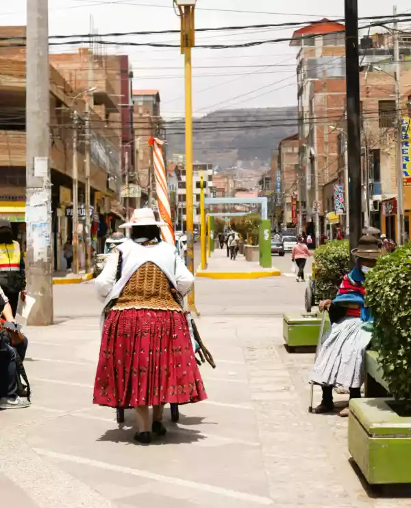 En dame iført tradisjonelt antrekk fra Ecuador, går langs et gangfelt i gatene i Puno.