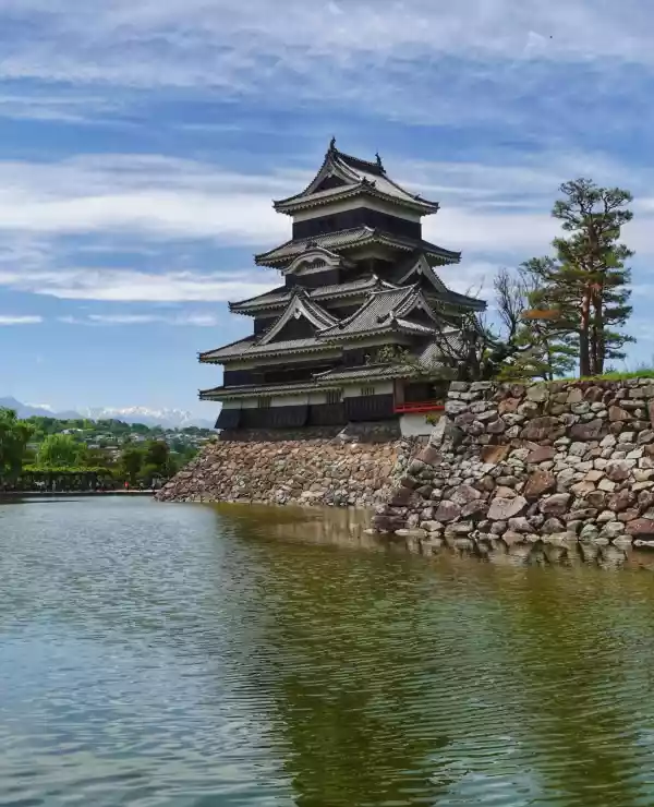 Matsumoto-slottet står majestetisk i sin tradisjonelle japanske arkitektur, vakkert beliggende ved bredden av en innsjø, omfavnet av frodige trær.