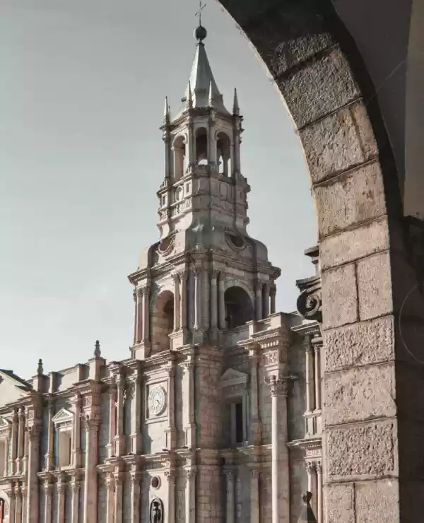 Et tårn i barokkstil i Arequipa, sett gjennom en betongbue. Den grå himmelen gir en dramatisk bakgrunn som fremhever tårnets detaljerte arkitektur og eleganse.