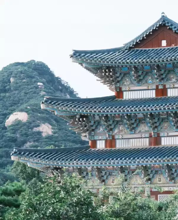 Tradisjonelt koreansk arkitektur, omgitt av frodig natur, fjell og grå himmel.